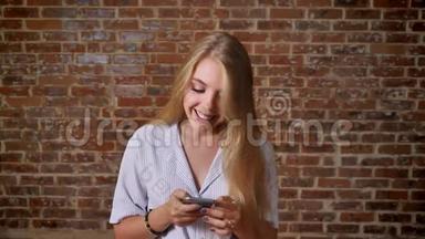 年轻的白种人金发美女使用智能手机显示智能手机屏幕、绿色屏幕、肖像、砖墙。